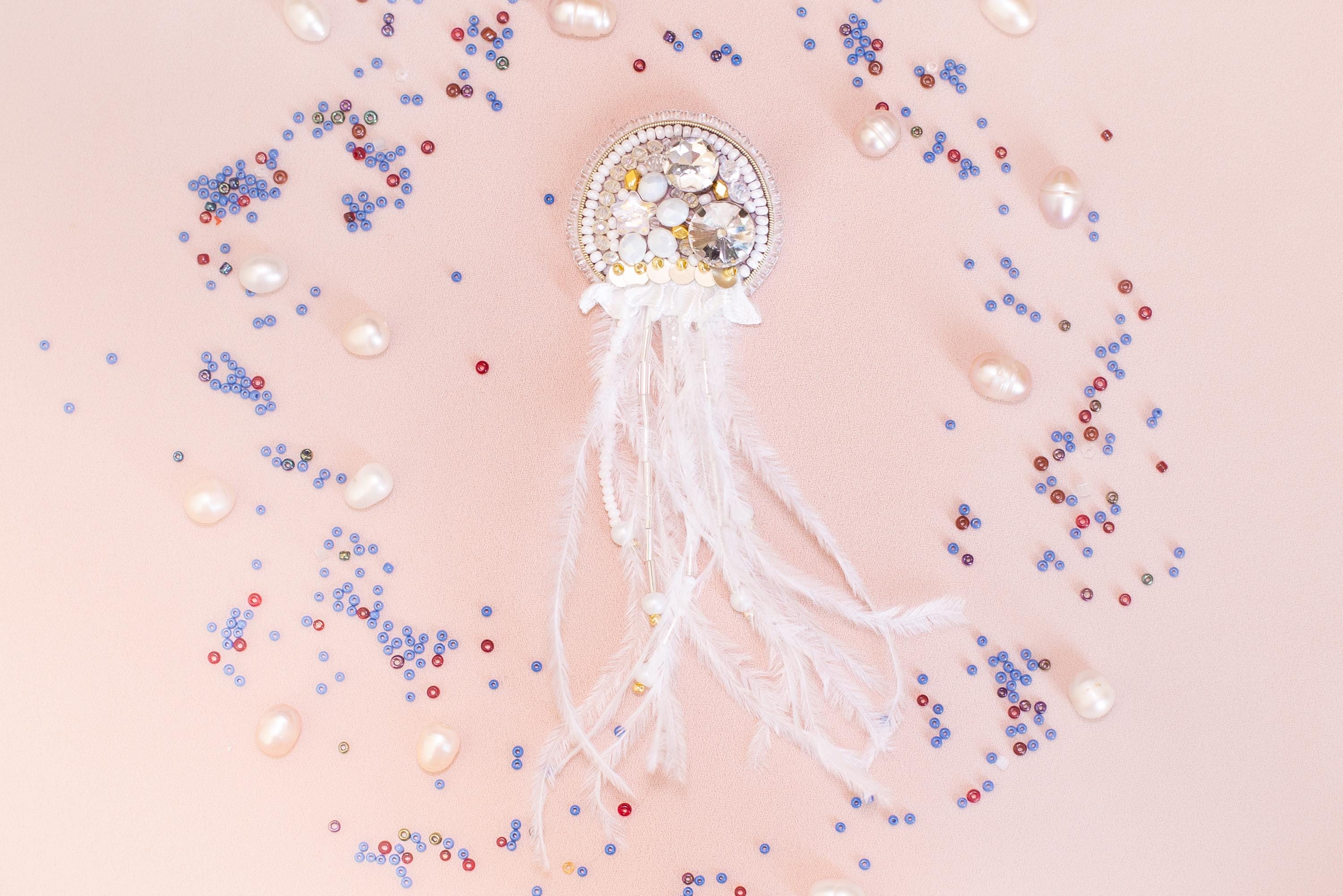 a decorative piece with a white and gold design, surrounded by various colorful beads and pearls on a light pink background.